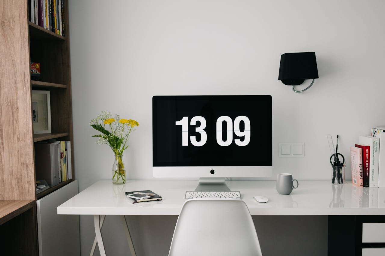 A minimalist workspace featuring a computer displaying time, organized bookshelves, and stylish decor.