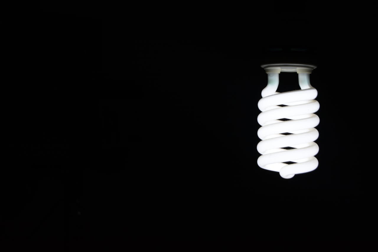 Bright spiral LED lightbulb against black background, artistic minimalism.